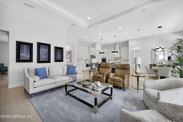 living room with light wood-type flooring, a chandelier, and a tray ceiling