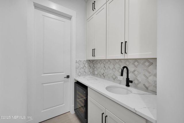 bathroom with sink, light stone counters, white cabinetry, wine cooler, and decorative backsplash