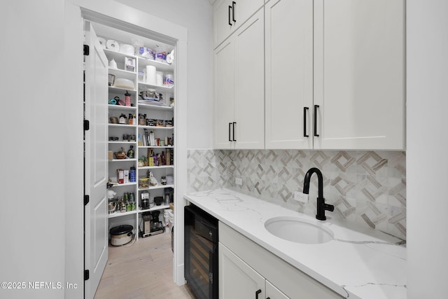 pantry with sink, beverage cooler, light hardwood / wood-style floors, white cabinets, and light stone countertops