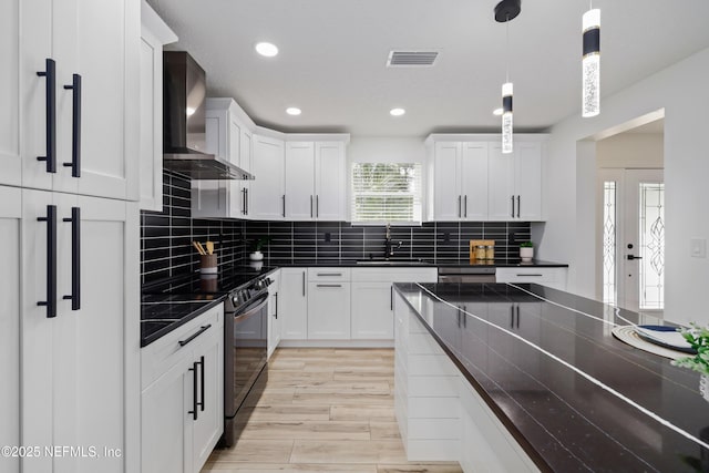 kitchen featuring wall chimney exhaust hood, black electric range oven, sink, decorative light fixtures, and backsplash