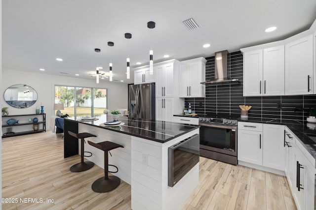 kitchen featuring white cabinetry, appliances with stainless steel finishes, decorative light fixtures, and wall chimney exhaust hood