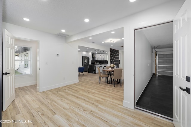 interior space with black fridge with ice dispenser and light hardwood / wood-style floors