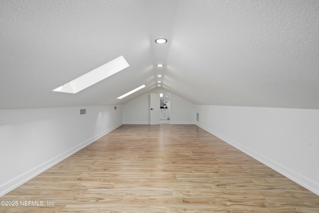 additional living space with light hardwood / wood-style flooring, lofted ceiling with skylight, and a textured ceiling