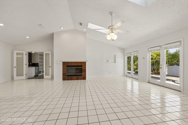 unfurnished living room with french doors, a textured ceiling, light tile patterned floors, a tile fireplace, and vaulted ceiling with skylight