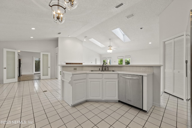 kitchen with sink, light tile patterned floors, lofted ceiling with skylight, white cabinets, and stainless steel dishwasher