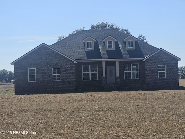 view of front of property with roof with shingles, a front lawn, and brick siding