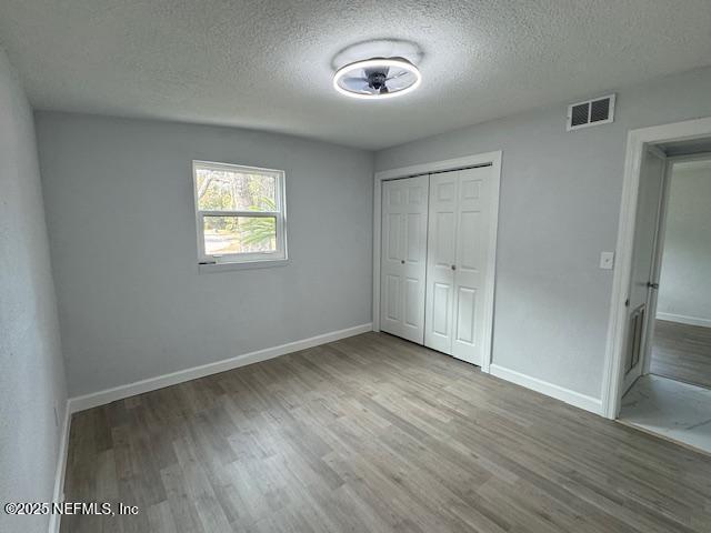 unfurnished bedroom featuring hardwood / wood-style flooring, a closet, and a textured ceiling