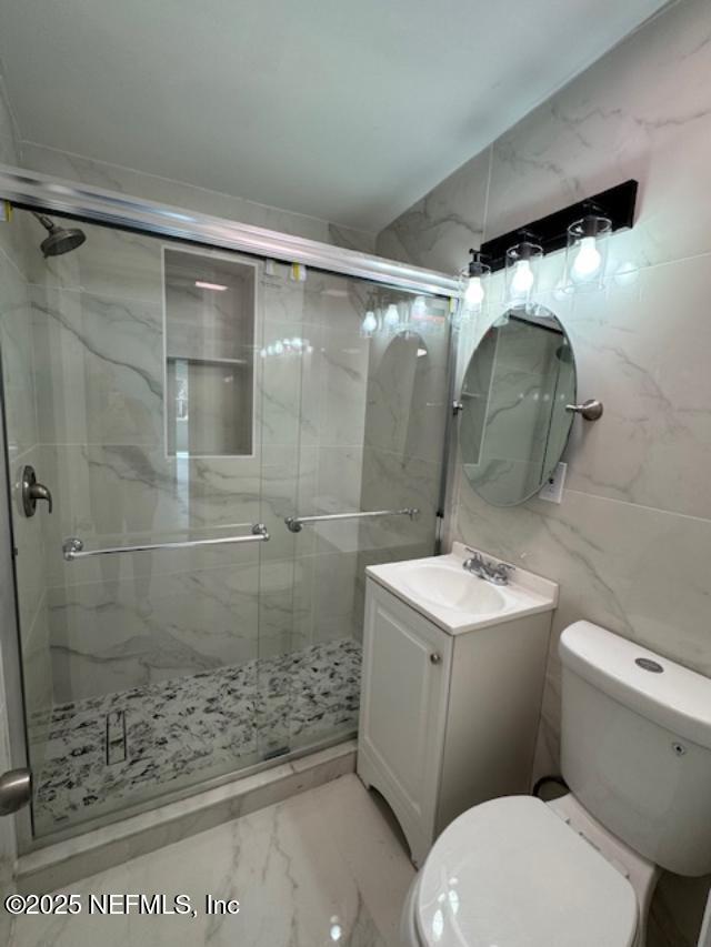 bathroom with a shower with door, vanity, tile walls, and toilet