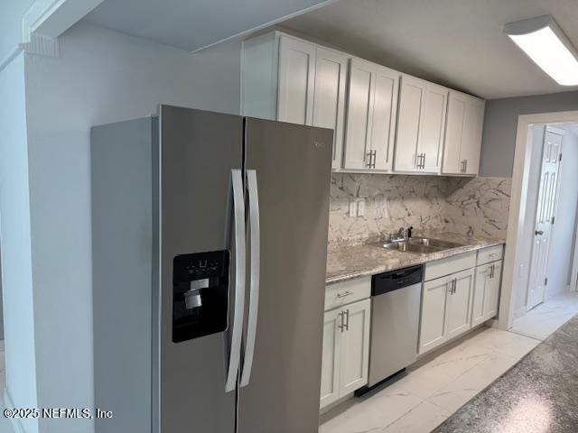 kitchen featuring sink, white cabinetry, stainless steel appliances, tasteful backsplash, and light stone countertops