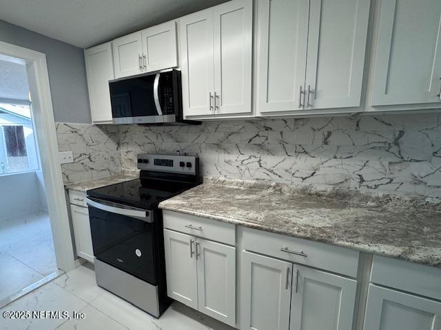 kitchen featuring light stone countertops, white cabinetry, appliances with stainless steel finishes, and backsplash