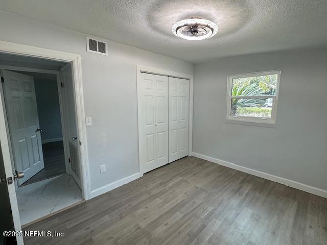 unfurnished bedroom with wood-type flooring, a textured ceiling, and a closet