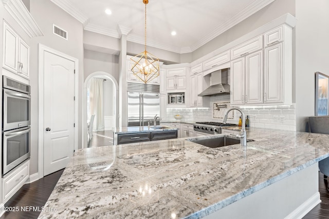 kitchen with pendant lighting, white cabinets, light stone counters, and wall chimney exhaust hood