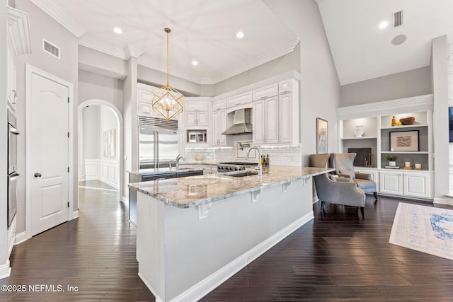 kitchen featuring hanging light fixtures, a breakfast bar, stainless steel appliances, and wall chimney exhaust hood