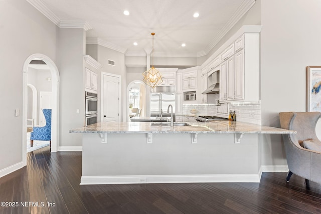 kitchen with decorative light fixtures, white cabinetry, light stone counters, kitchen peninsula, and wall chimney range hood