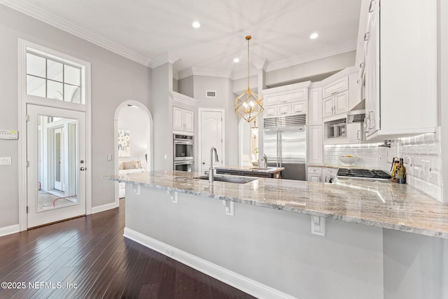 kitchen featuring sink, white cabinetry, built in appliances, decorative light fixtures, and kitchen peninsula