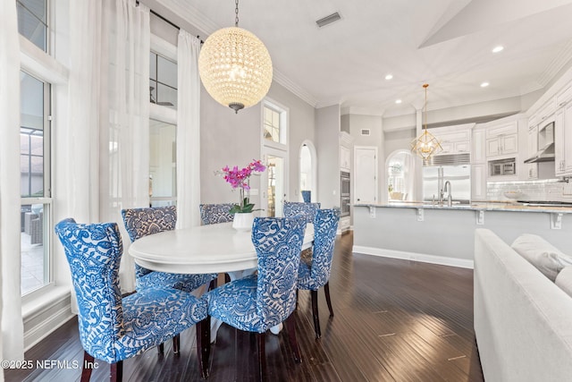 dining area featuring dark hardwood / wood-style flooring, a notable chandelier, crown molding, and sink