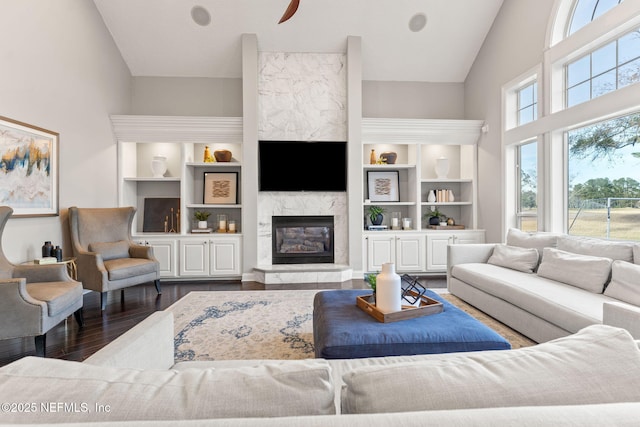 living room with dark wood-type flooring, a high end fireplace, built in shelves, and high vaulted ceiling