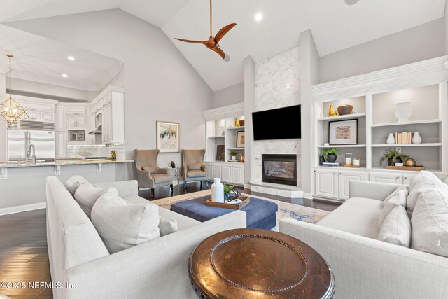 living room with sink, high vaulted ceiling, dark hardwood / wood-style floors, a high end fireplace, and ceiling fan with notable chandelier