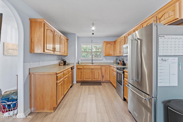 kitchen with appliances with stainless steel finishes, sink, light wood-type flooring, light brown cabinets, and a textured ceiling