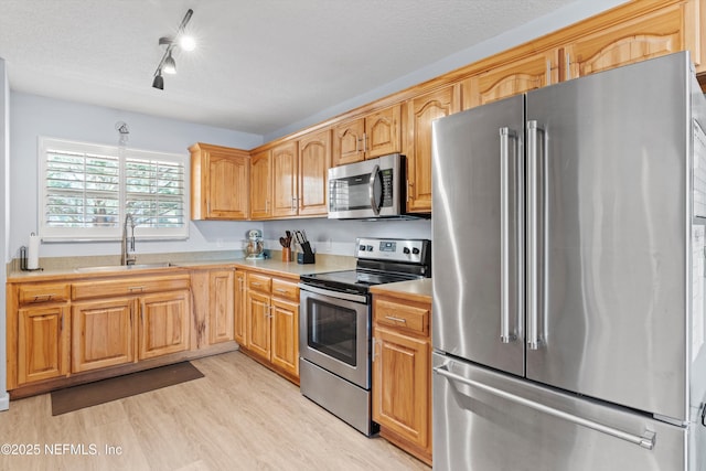 kitchen with stainless steel appliances, sink, a textured ceiling, and light wood-type flooring