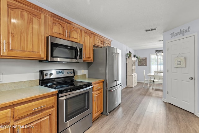 kitchen featuring appliances with stainless steel finishes, light hardwood / wood-style floors, and a textured ceiling