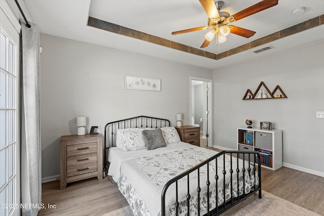 bedroom featuring ceiling fan, a tray ceiling, and light hardwood / wood-style flooring