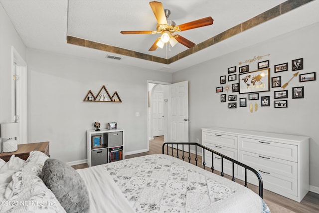 bedroom with a tray ceiling, ceiling fan, and light wood-type flooring