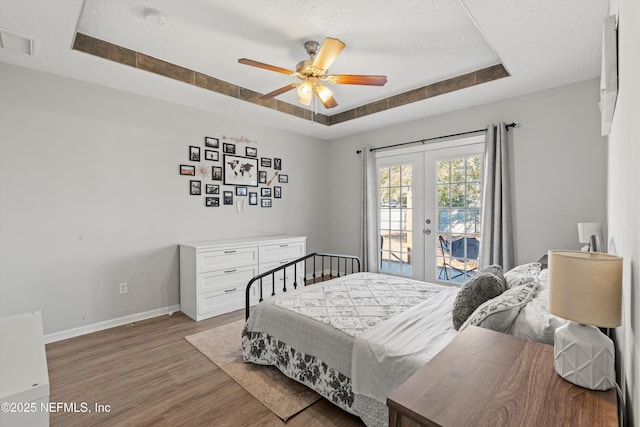 bedroom featuring ceiling fan, access to exterior, hardwood / wood-style floors, a tray ceiling, and french doors