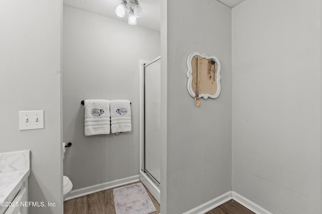 bathroom featuring hardwood / wood-style flooring, vanity, a textured ceiling, a shower with shower door, and toilet