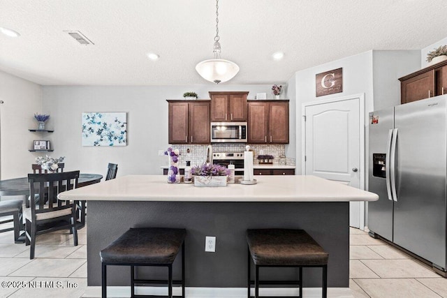 kitchen with appliances with stainless steel finishes, pendant lighting, a kitchen breakfast bar, decorative backsplash, and light tile patterned floors