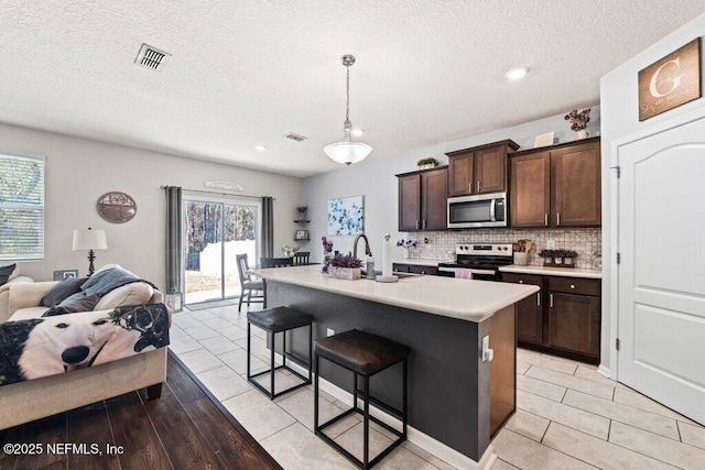 kitchen with pendant lighting, sink, stainless steel appliances, an island with sink, and decorative backsplash