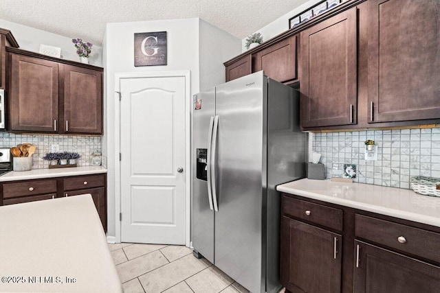 kitchen featuring stainless steel fridge, dark brown cabinetry, a textured ceiling, light tile patterned flooring, and decorative backsplash