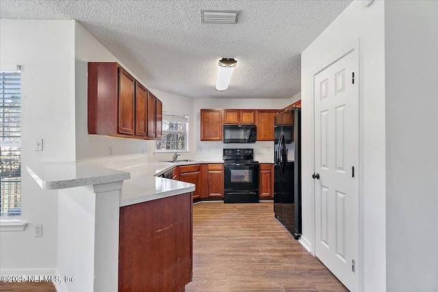 kitchen with sink, a textured ceiling, light hardwood / wood-style flooring, kitchen peninsula, and black appliances