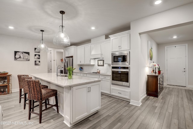 kitchen with stainless steel appliances, white cabinetry, light wood finished floors, and decorative backsplash