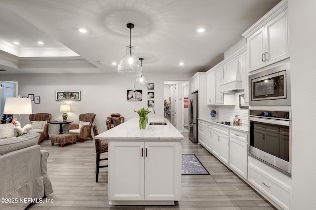 kitchen featuring a breakfast bar area, stainless steel appliances, open floor plan, light wood finished floors, and custom range hood