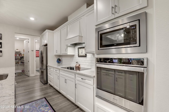 kitchen with custom exhaust hood, decorative backsplash, appliances with stainless steel finishes, white cabinets, and wood finished floors