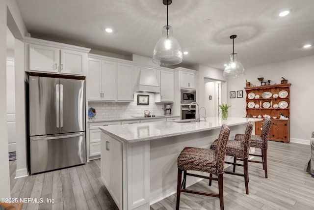 kitchen with stainless steel appliances, white cabinets, custom range hood, light wood finished floors, and tasteful backsplash