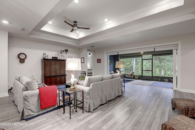 living area featuring a tray ceiling, visible vents, ornamental molding, ceiling fan, and wood finished floors