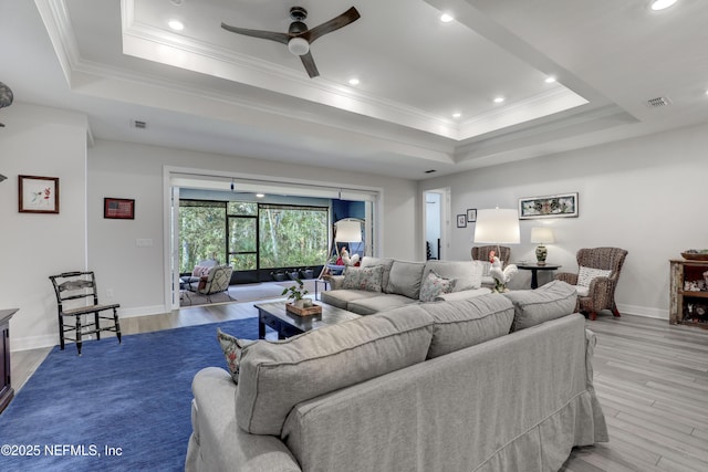 living room with a raised ceiling, visible vents, crown molding, and wood finished floors