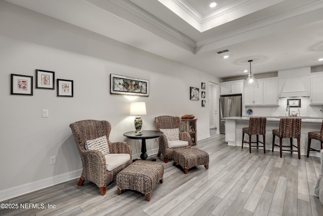 sitting room featuring light wood-style floors, baseboards, a tray ceiling, and crown molding