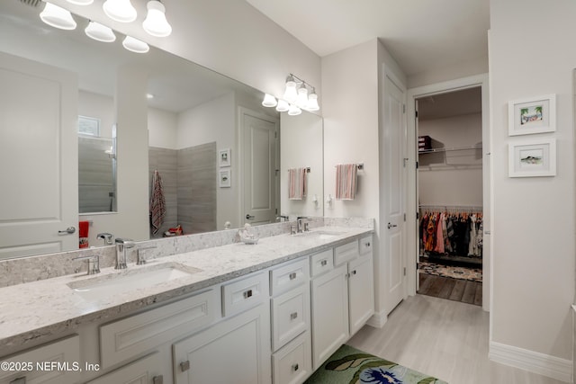 full bath featuring wood finished floors, a spacious closet, double vanity, and a sink