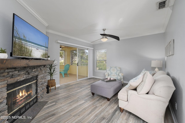 living room featuring crown molding, ceiling fan, a stone fireplace, and hardwood / wood-style floors