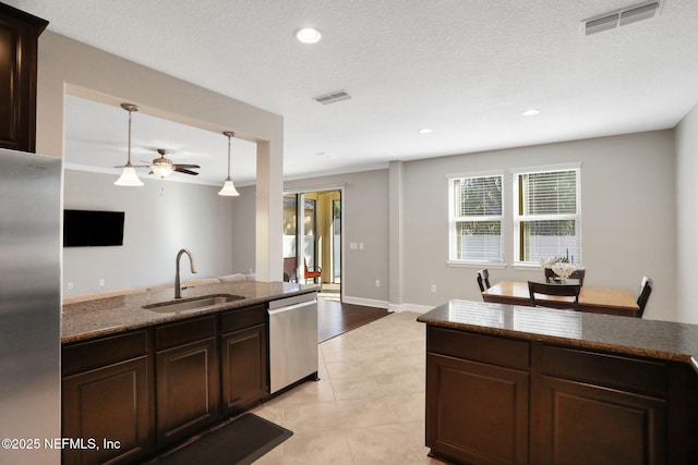 kitchen with appliances with stainless steel finishes, sink, dark stone countertops, and dark brown cabinetry