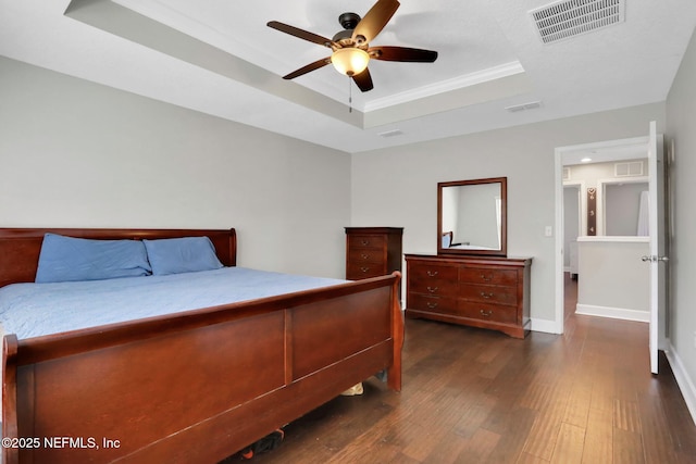 bedroom with dark wood-type flooring, ceiling fan, and a tray ceiling