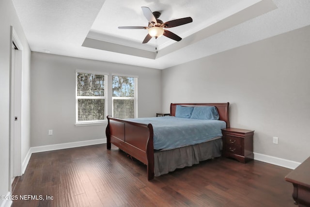 bedroom with a textured ceiling, dark wood-type flooring, a raised ceiling, and ceiling fan