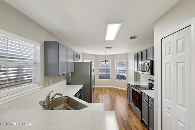 kitchen featuring pendant lighting, sink, appliances with stainless steel finishes, gray cabinetry, and a notable chandelier