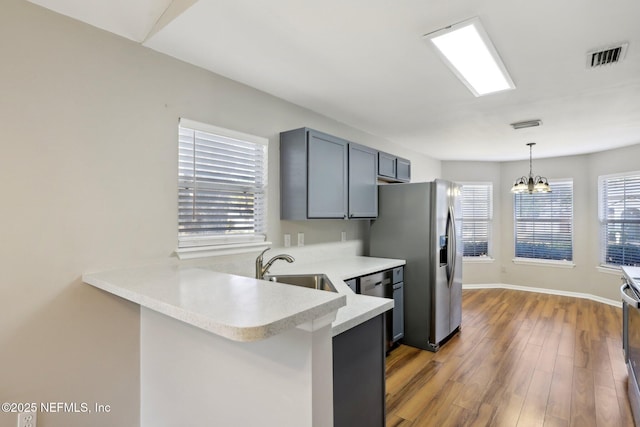 kitchen with appliances with stainless steel finishes, pendant lighting, sink, kitchen peninsula, and light hardwood / wood-style flooring