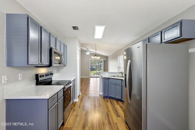 kitchen with lofted ceiling, sink, decorative light fixtures, stainless steel appliances, and hardwood / wood-style floors