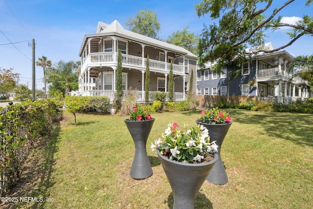 exterior space featuring covered porch, a balcony, a front yard, and metal roof