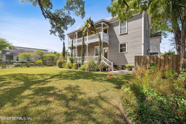 rear view of property featuring a balcony, fence, and a yard